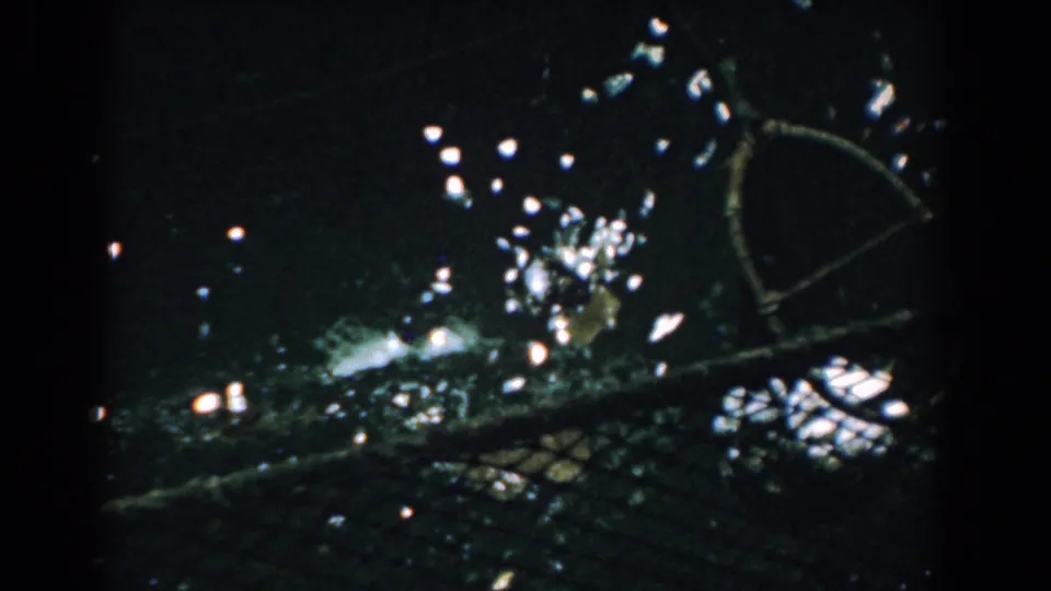 1958 Yorktown 8mm frame showing wet debris, netting, and rope-framed gear glistening against very dark water.