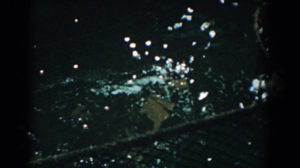 1958 Yorktown 8mm frame showing tangled netting and debris in dark rippling water with strong light reflections.