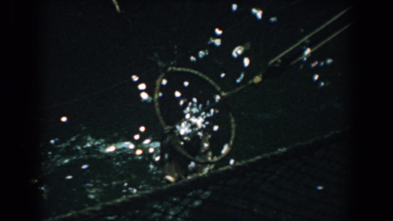 1958 Yorktown home-movie frame showing a dark exterior detail with a circular metal form, diagonal rods, and scattered light reflections.