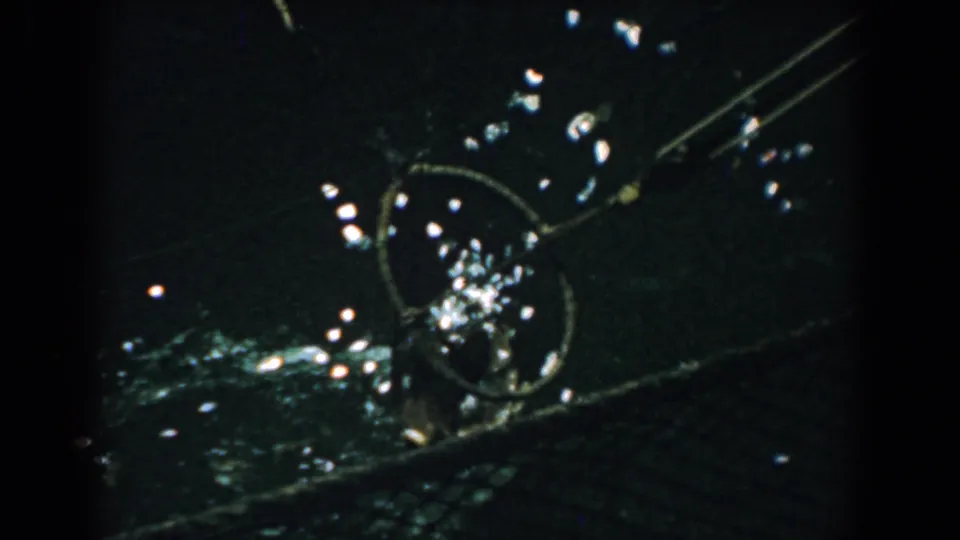 1958 Yorktown home-movie frame showing a dark exterior detail with a circular metal form, diagonal rods, and scattered light reflections.