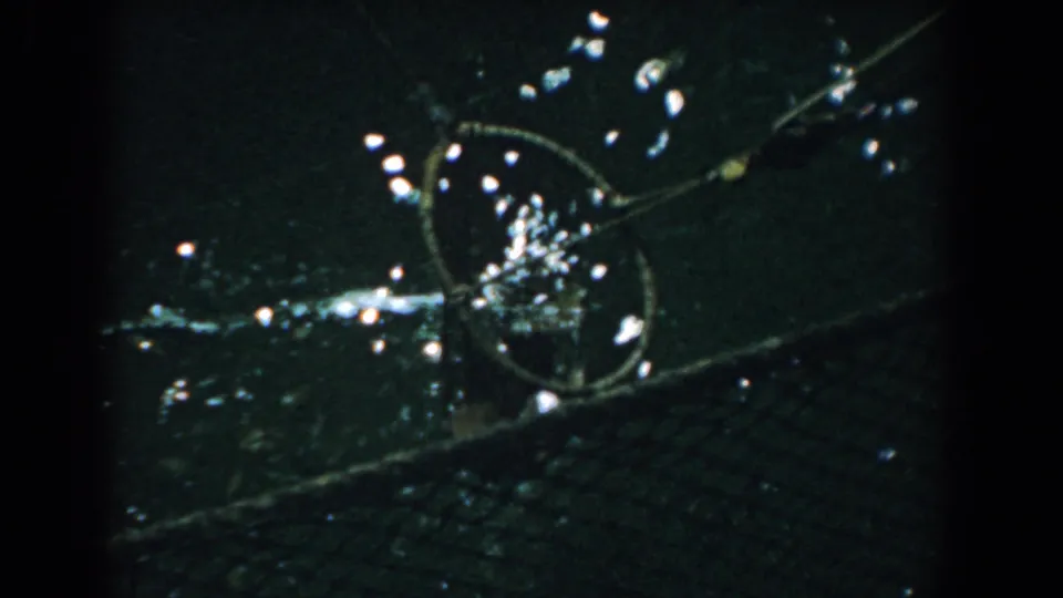 1958 Yorktown home-movie still showing a shadowed close view of a circular metal element with reflections and a textured lower band.