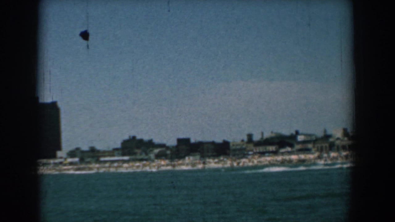 Distant shoreline and dark waterfront buildings seen across blue water.