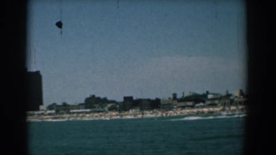 1958 Yorktown, Virginia home-movie frame showing a distant shoreline, beach, and dark buildings across the water.
