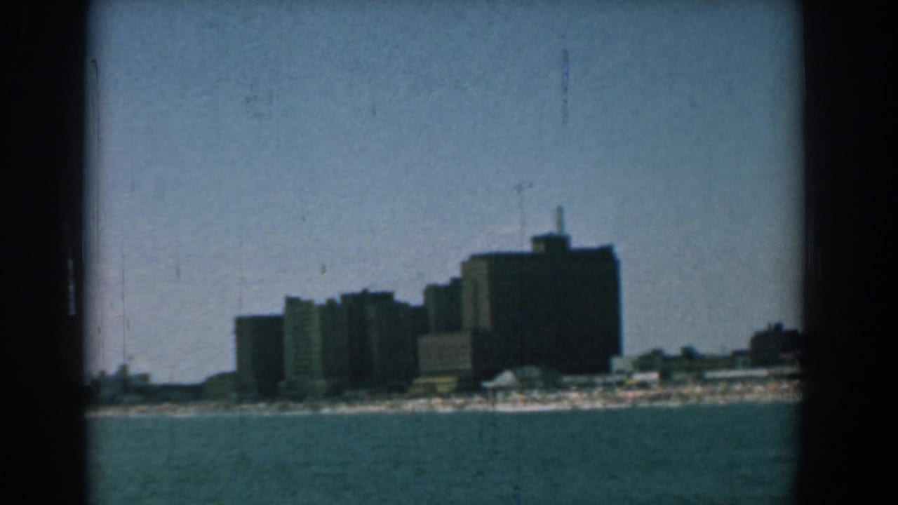 Distant grey building complex across blue-green water under a pale sky.