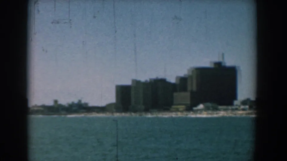 Soft 8mm frame of Yorktown waterfront buildings and a low beach area viewed from across blue-green water.