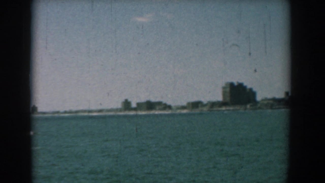 Distant shoreline buildings across blue-green water under a pale sky.