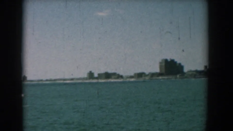 1958 Yorktown, Virginia home-movie frame showing distant coastal buildings across open water with visible 8mm frame edges.