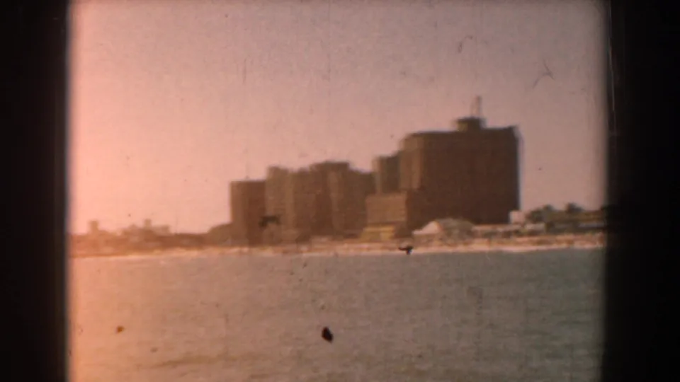 A warmer, faded 8mm frame shows the same distant waterfront buildings across calm water near the end of the clip.