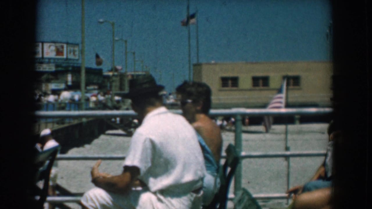 Young adults seated on benches beside a boardwalk railing under a blue sky.