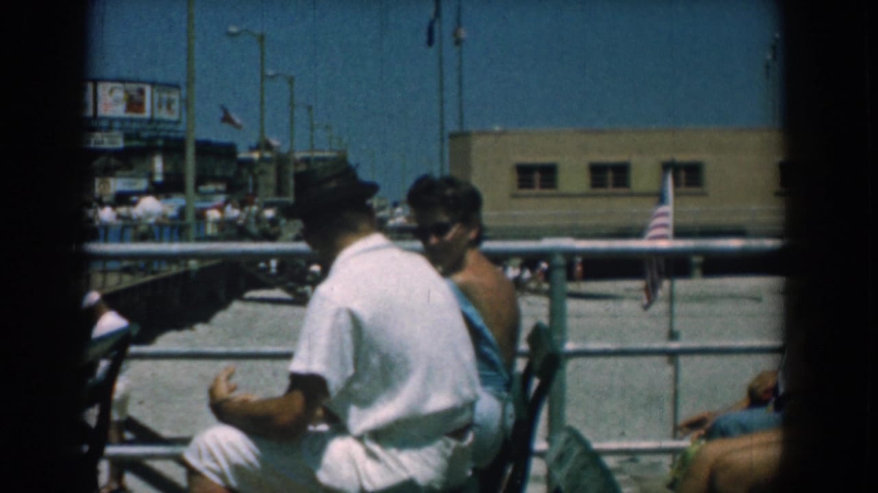 A man in white and a woman in a blue dress sit near the railing during a 1958 Yorktown, Virginia public outing.