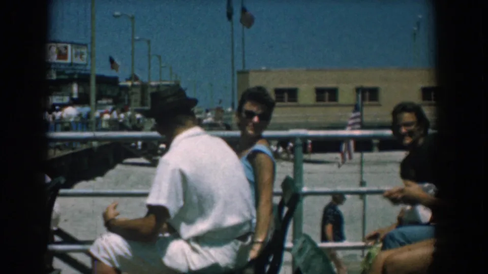 Two women look toward the camera as a seated man faces away on a bright 1958 Yorktown, Virginia boardwalk scene.