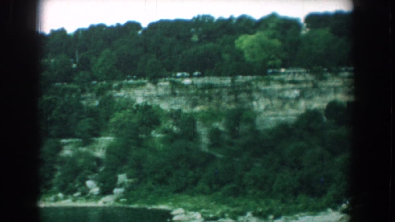 Tree-lined quarry wall with brush and a road or path near the lower edge.