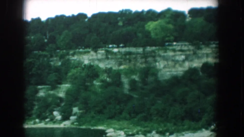 Yorktown quarry landscape with a wooded ridge, pale rock face, vegetation, and a small road or path near the bottom of frame.