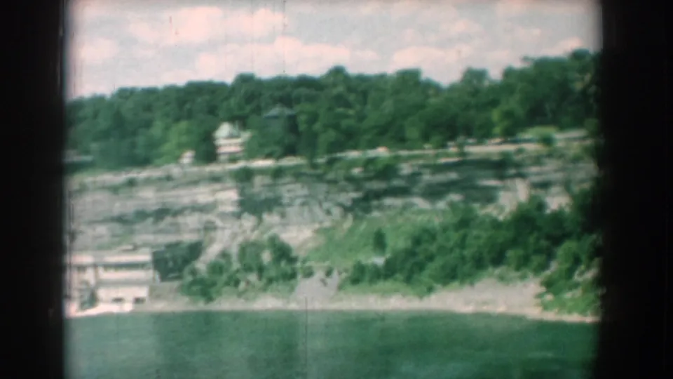 Wide view of the Yorktown quarry swimming hole, showing calm water, pale rock walls, wooded slopes, and small ridge-top structures.