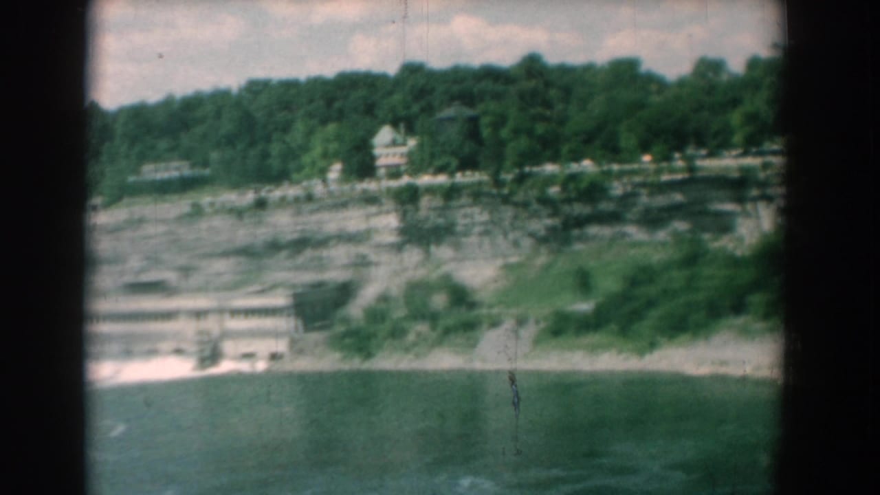 1958 Yorktown, Virginia 8mm frame showing a river, layered cliff face, trees, and small buildings on the ridge.