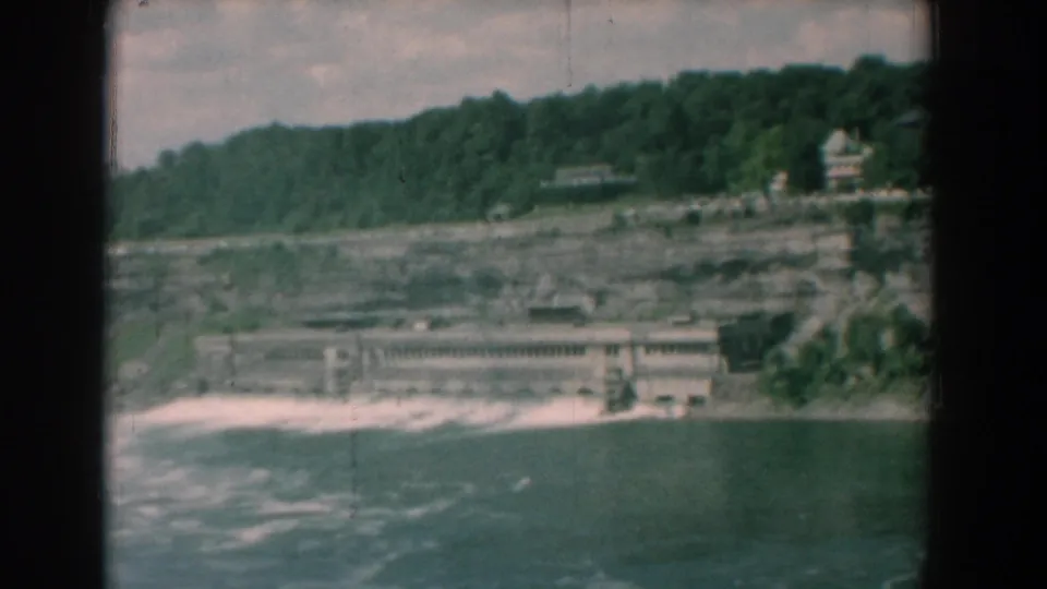 Final 1958 Yorktown river frame with rippled water, a shoreline structure, cliffside terrain, and trees on the ridge.