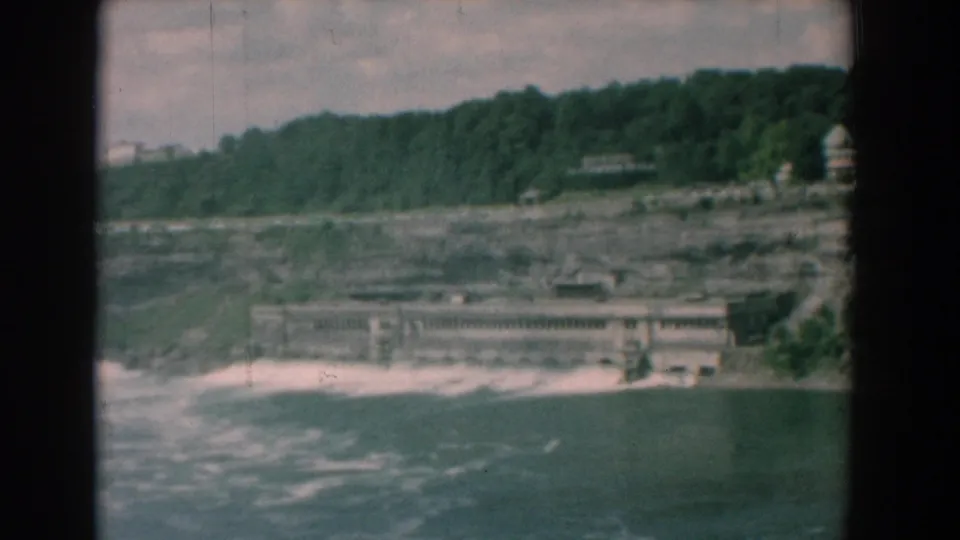 Wide 8mm view of a Yorktown-area river scene with a low concrete structure, rocky slope, and dense treeline above.