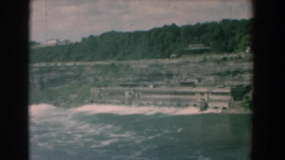 1958 home-movie frame of river rapids or falls below a concrete riverside wall and wooded hillside in Yorktown, Virginia.