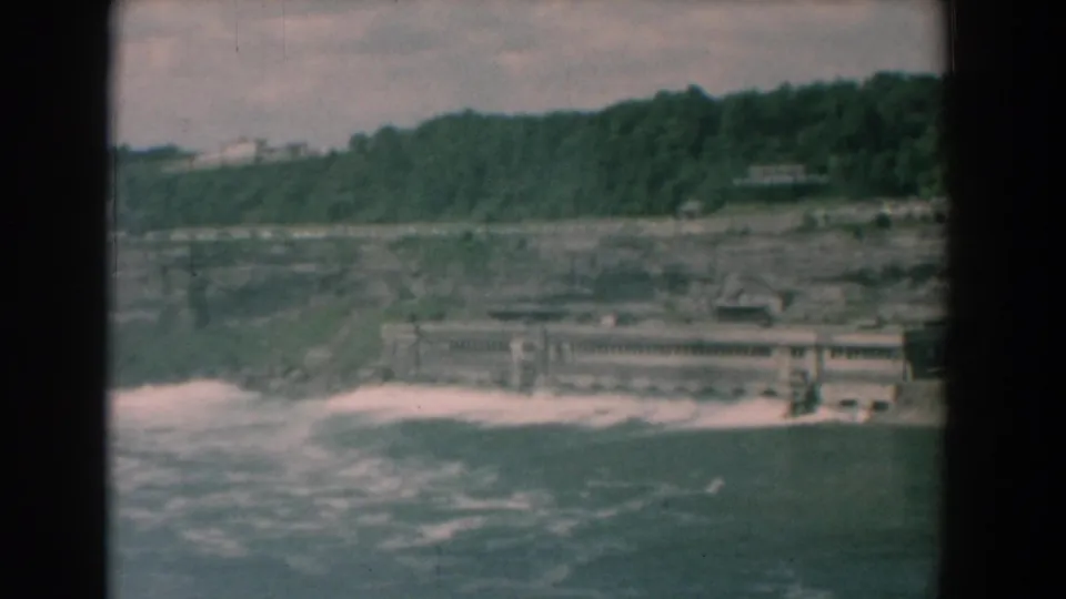 Faded 8mm frame from 1958 showing a Yorktown river, whitewater, concrete structure, rocky shore, and wooded bluff.