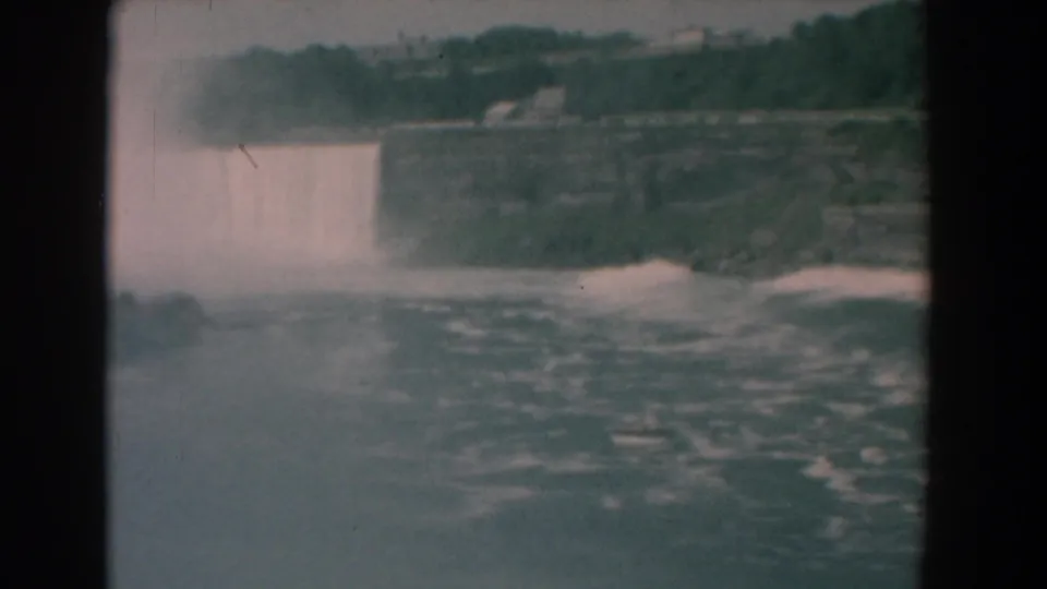 Faded 1958 8mm view from Yorktown, Virginia, with a broad water drop, spray cloud, rocky shoreline, and turbulent river water.