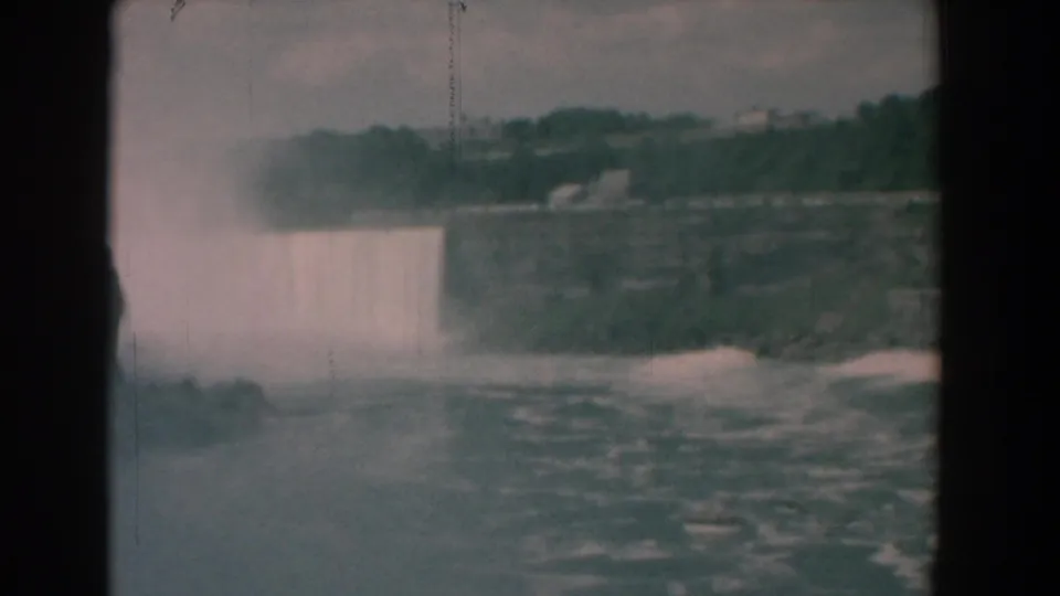 1958 8mm Yorktown, Virginia frame showing a wide cascade, heavy spray, foaming river water, rocky bank, and tree-covered background.