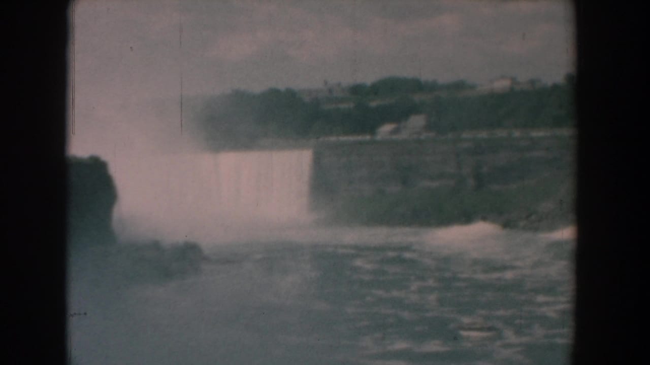 Large waterfall viewed across churning water with mist and dark rock borders.