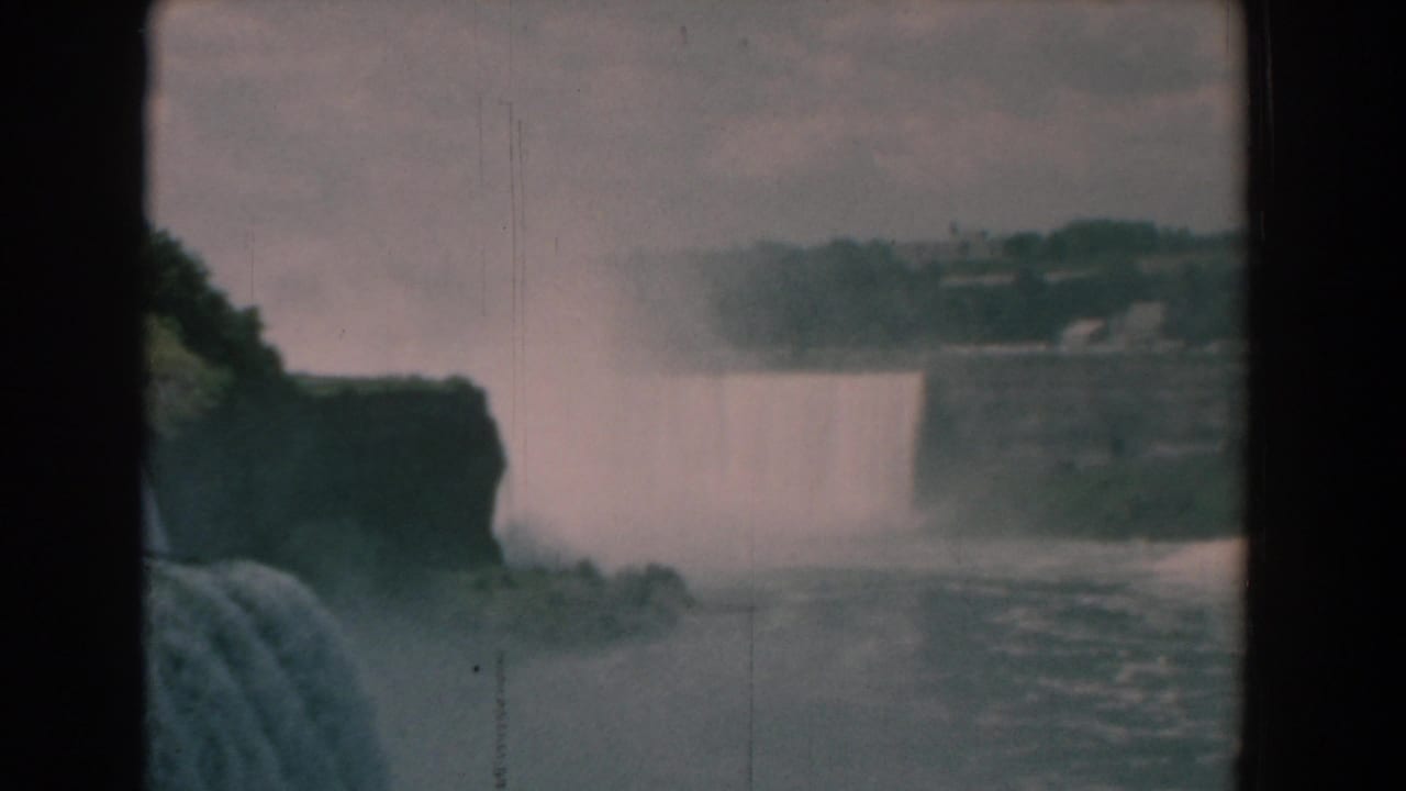 Distant waterfall viewed through dark film borders with mist and cliffs.
