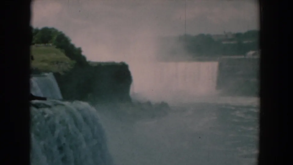 Soft 8mm frame of a waterfall landscape, with heavy mist covering much of the distant falls and riverbank.