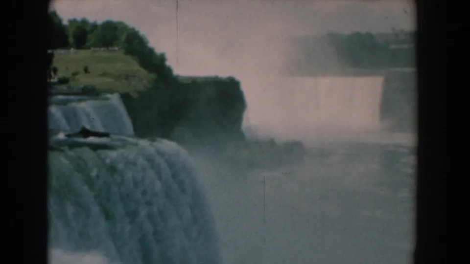 1958 8mm frame with foreground cascade, distant waterfall curtain, mist, and a green bluff above the river.