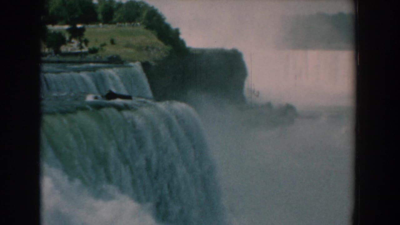 Waterfall crest and mist with a grassy, tree-lined bluff above.