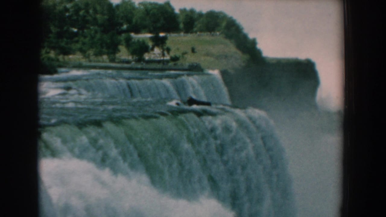 Water pours over a broad waterfall with trees along the cliff edge and mist below.