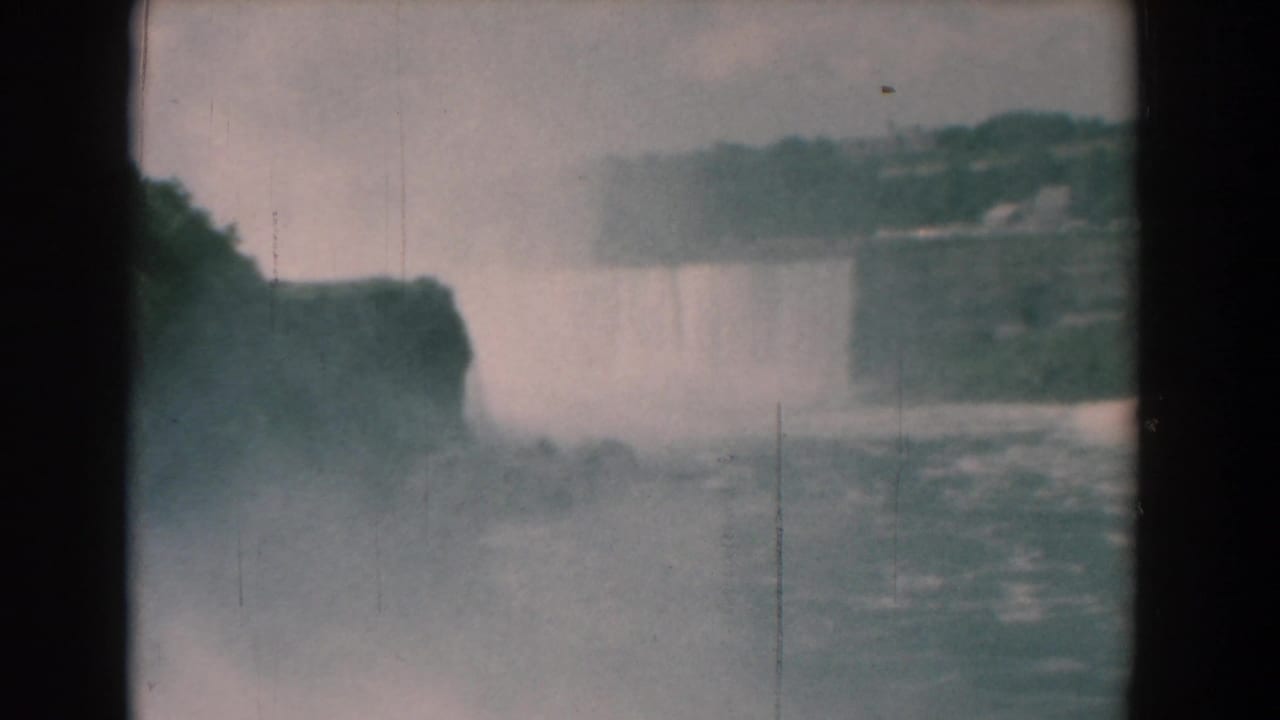 Distant waterfall and mist fill the gorge, with dark cliffs and river water visible.