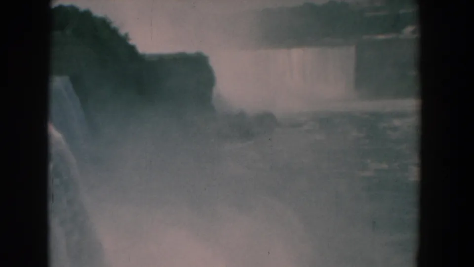 1958 8mm travel frame of Niagara Falls with heavy mist, river water, and a distant waterfall across the gorge.