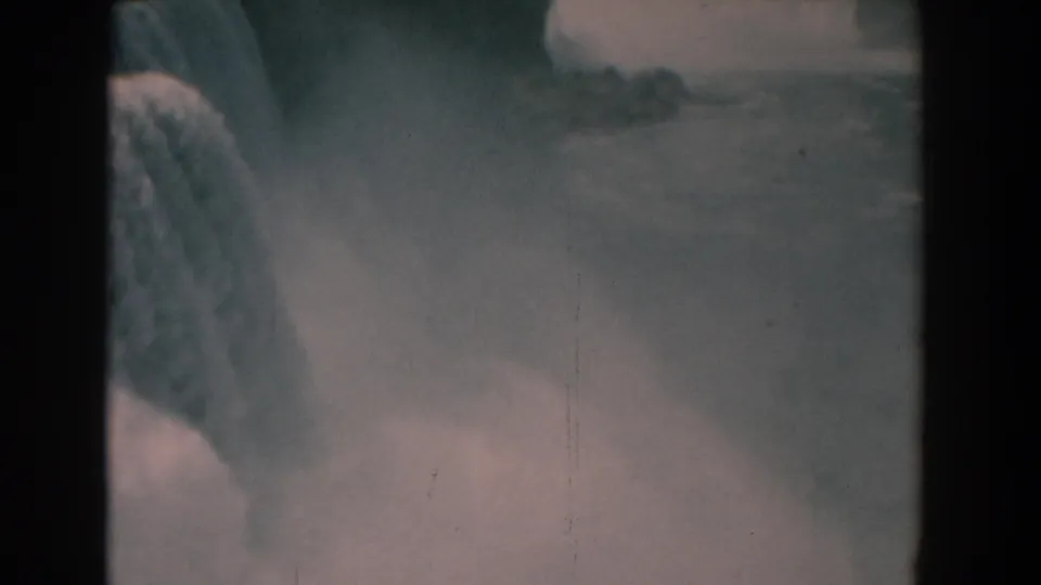 1958 8mm home-movie frame showing the waterfall edge, spray, and river below in faded color.