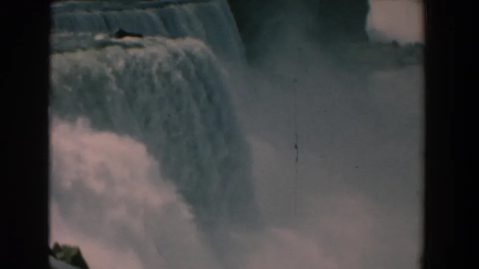 1950s home-movie frame of American Falls, showing textured water spilling over the brink and pale mist below.