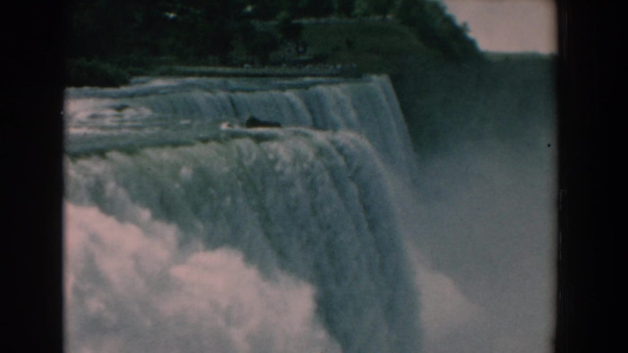 Waterfall edge with foaming water, mist at right, and trees beyond the brink.