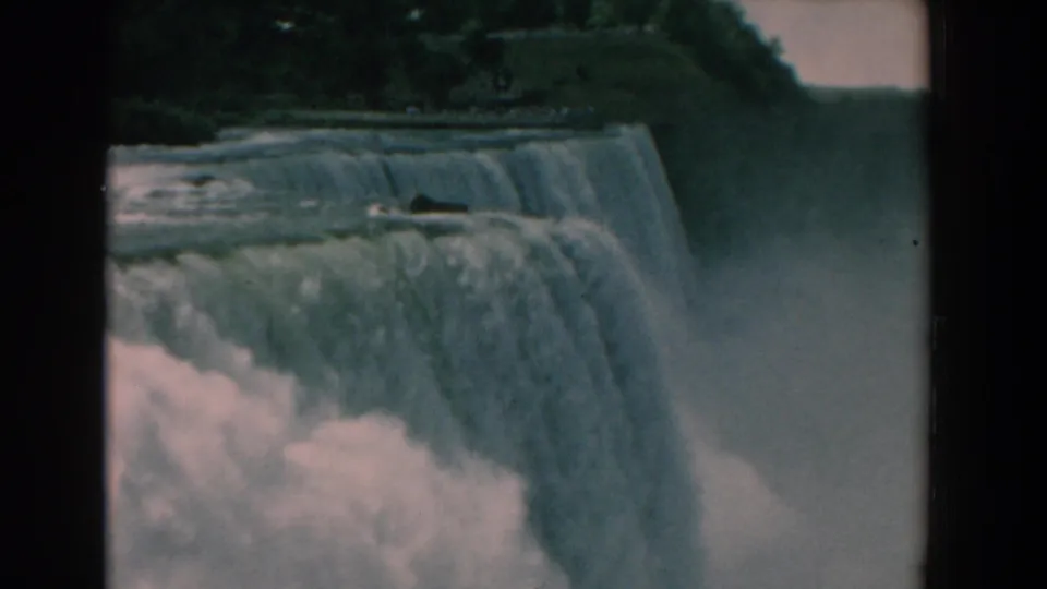 1958 8mm view of a waterfall crest and falling water, with a dark tree line and mist softening the right side.