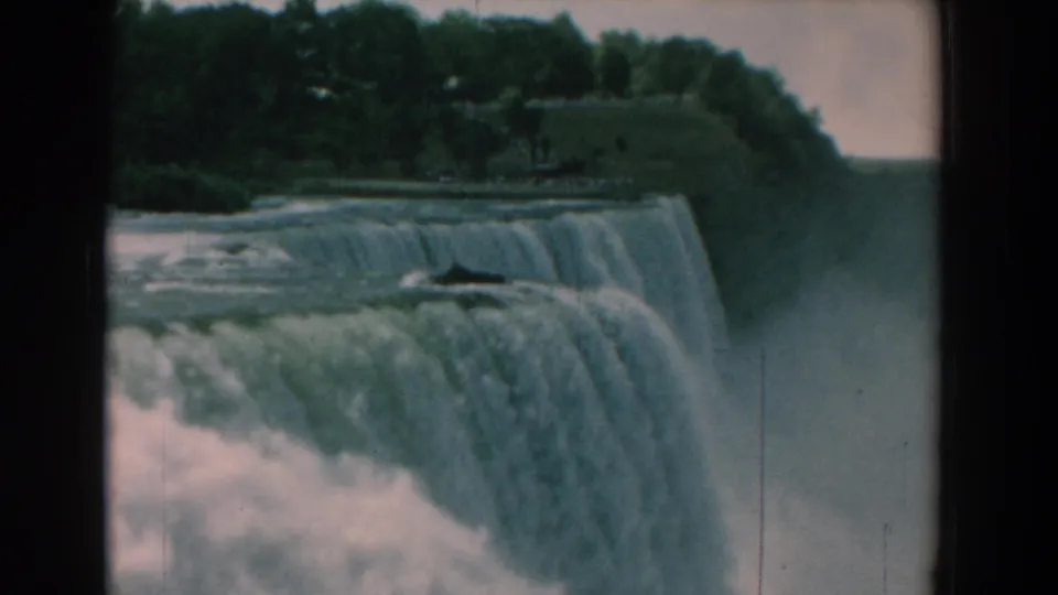 1958 8mm frame showing a waterfall from a slightly shifted angle, with the far bank, trees, and mist visible.
