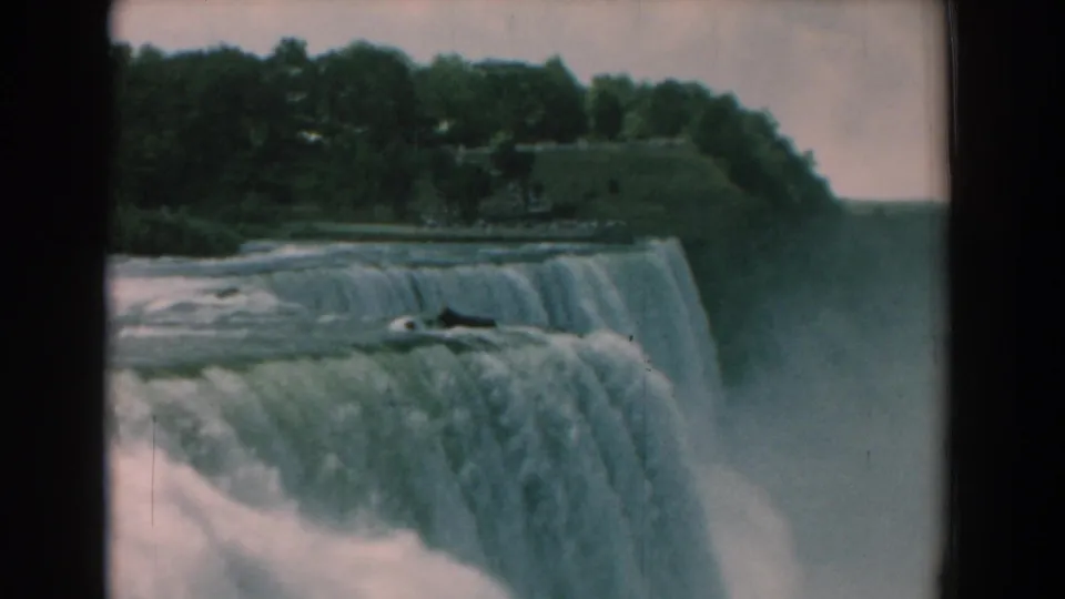1958 8mm frame of the falls and surrounding greenery, with water spilling over the brink into a misty basin.