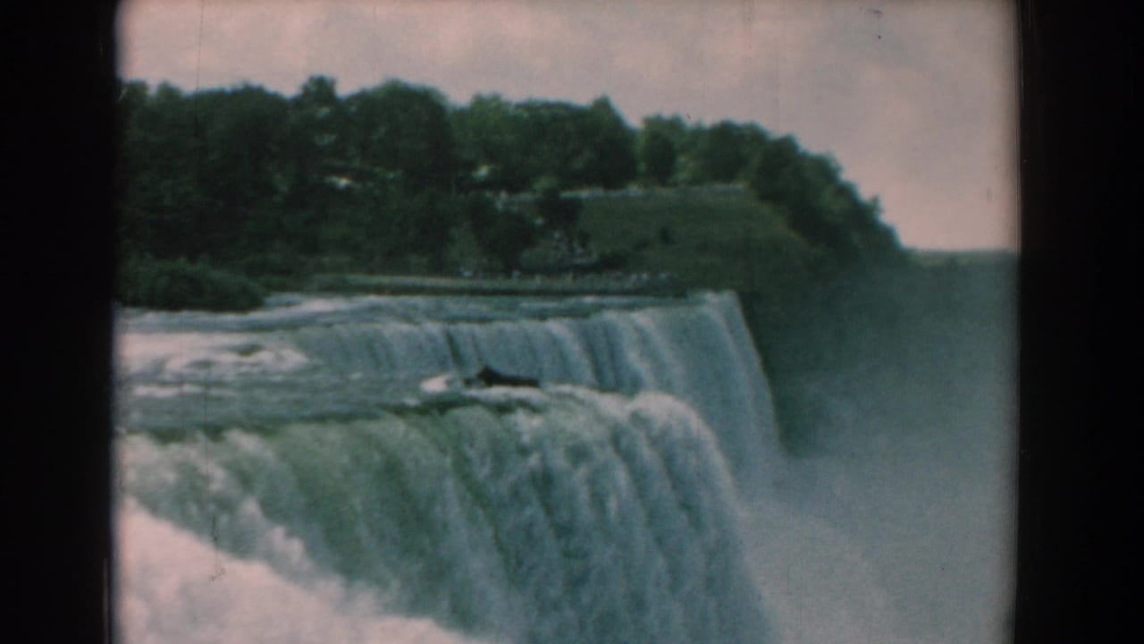 Broad waterfall spilling over a cliff with trees above and mist rising below.