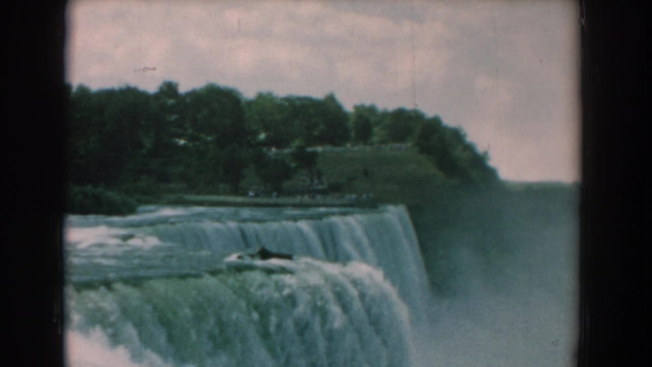 Waterfall edge seen from a high angle with trees and mist in the distance.