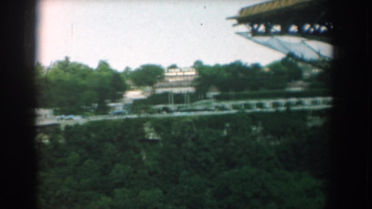 Similar elevated view of trees, roadside structures, vehicles, and a large roof edge at the upper right.