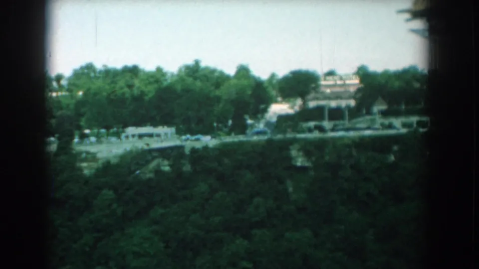 Final Yorktown frame showing a leafy roadside, passing vehicles, low structures, and a large roof edge in soft 1958 8mm color.
