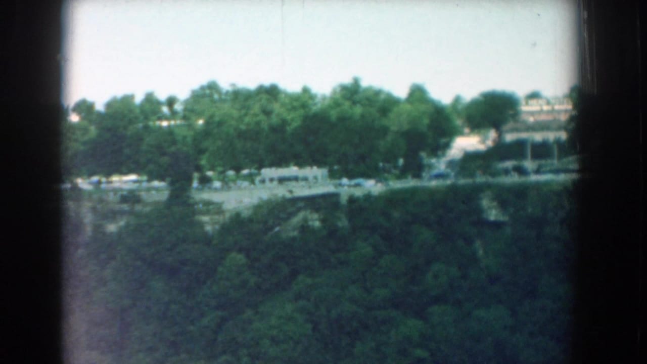 Distant town view above dense trees with heavy film gate shadows.