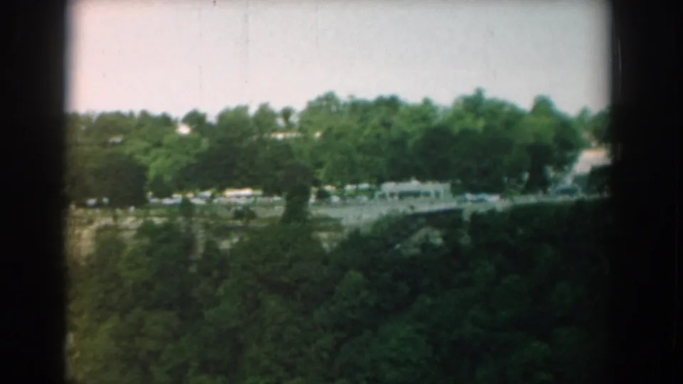 Final 1958 Yorktown frame showing a wooded slope, pale roadway, distant structures, sky, and the dark borders of the 8mm film scan.