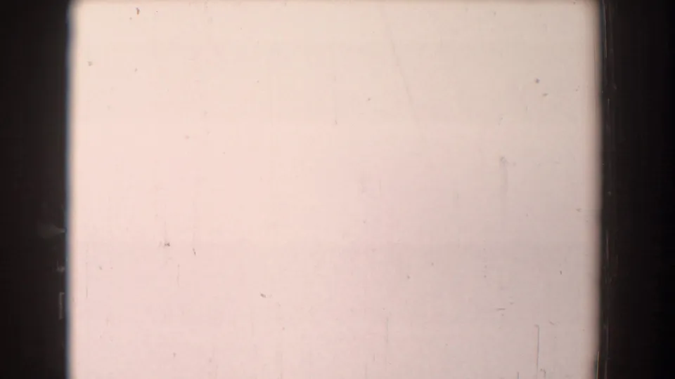 Pale overexposed or leader-like 8mm frame from the Yorktown clip, with dark film edge, dust specks, and faint vertical marks.