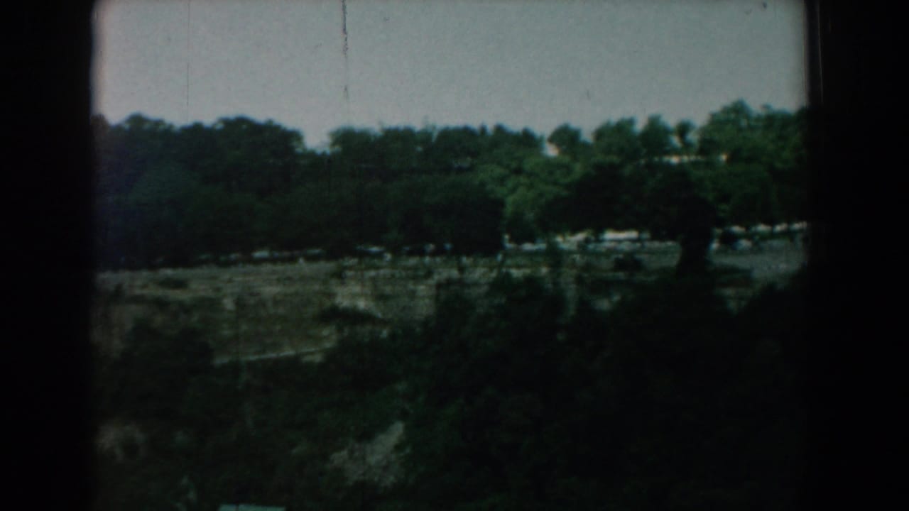 Dark wooded landscape with distant pale figures and heavy black film borders.