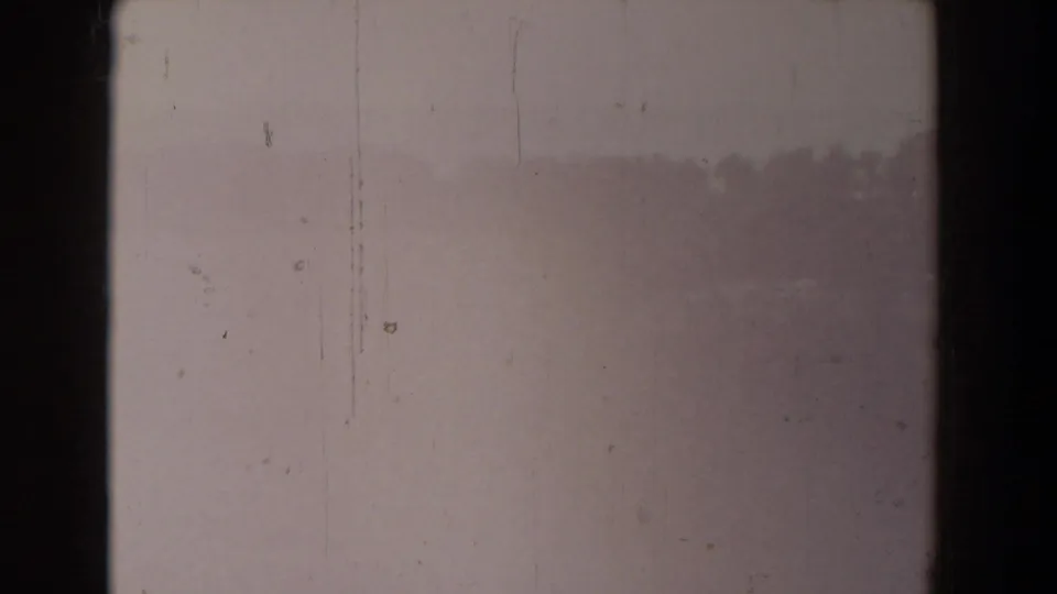 A faded 8mm frame with pale exposure, vertical scratches, dust marks, and only faint suggestion of the outdoor scene.