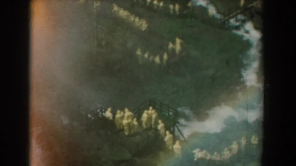 Wide 1958 Yorktown frame with a long distant line of yellow-robed figures moving across a wooded, uneven landscape.