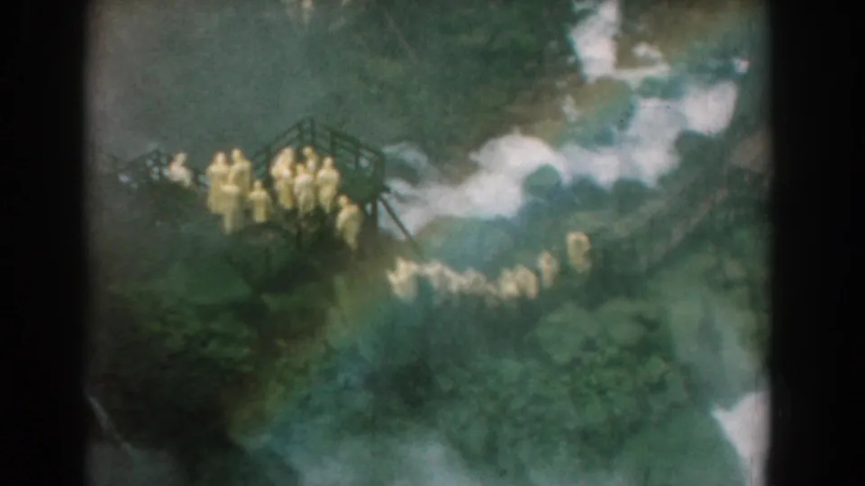 A wider 1958 home-movie view shows people on and below a wooden platform in a green wooded area near Yorktown, Virginia.